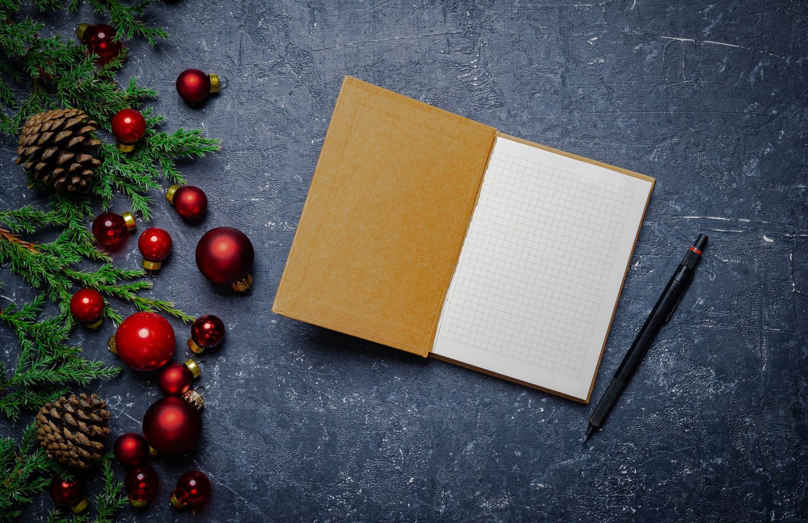 Aufgeschlagenes Notizbuch mit Tannenzweigen und roten Weihnachtskugeln zum Planen der Adventszeit